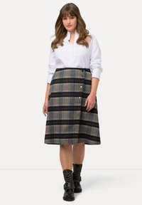 Geruite knie-lange rok in donkerblauw en beige tinten, met een knoopsluiting aan de zijkant, gecombineerd met een witte blouse met kraag en zwarte laarzen.