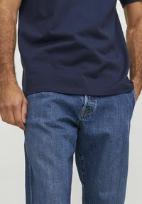 T-shirt in cotone blu navy con vestibilità rilassata, abbinato a jeans in denim azzurro chiaro con una leggera texture e design classico a cinque tasche.