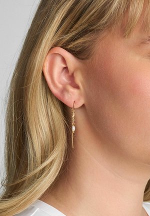 Cercei aurii agățați prezintă un lanț subțire cu un accent de perlă albă. Designul este delicat, evidențiind forme geometrice minimaliste.