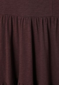 Maroon tkanina s mekanim teksturom i nabranim detaljima na rubu, što stvara slojeviti izgled. Lagana je i slobodno pada.