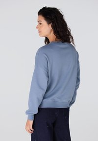 Lichtblauw sweatshirt met een ontspannen pasvorm, brede lange mouwen en geribde zoom. Zacht materiaal met een gladde textuur, weergegeven vanaf de achterkant.