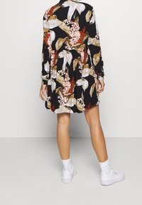 Czarna sukienka w kwiatowe wzory w odcieniach beżu, różu i czerwieni. Długie rękawy, marszczona talia i rozkloszowana spódnica. Noszona z białymi trampkami.