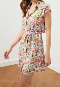 Sukienka z krótkim rękawem w kolorowy kwiatowy wzór, z kołnierzykiem, zapinana na guziki z przodu oraz z paskiem w talii. Wykonana z lekkiego materiału.