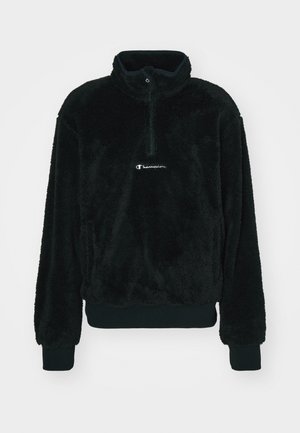 Suéter de forro polar negro con cuello alto, cierre de media cremallera, puños elásticos y un pequeño logo blanco en la parte frontal. Textura suave en toda su superficie.