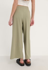 Lichtgroene, geribbelde wijde broek met een elastische tailleband. De stof heeft een subtiele textuur. G gedragen met zwarte platform sandalen.