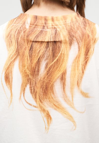 Vista traseira de uma pessoa vestindo uma camisa branca com estampa realista de cabelo longo e ondulado em vermelho, que se estende pelas costas.