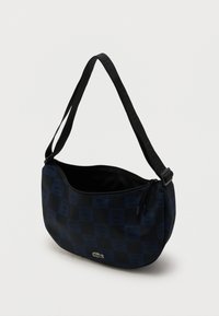 Rame in mornarsko modra karo ramenska torbica z vzorcem logotipa Lacoste, nastavljivim trakom in zgornjim odprtjem z zadrgo, prikazana delno odprta.