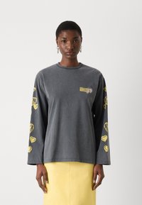 Gray long-sleeve shirt featuring yellow heart patterns on the sleeves and a small logo on the chest. Made of soft, textured fabric.