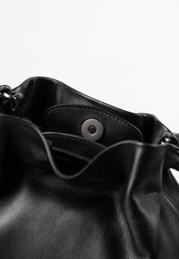 Schwarze Lederhandtasche mit Magnetverschluss, die strukturiertes Material und oben teilweise geöffnet zeigt vor einem schlichten weißen Hintergrund.