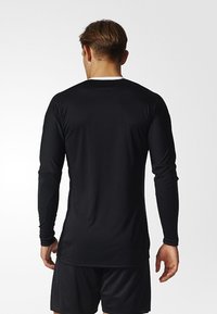 Chemise de sport noire à manches longues au design ajusté, avec un col rond et un tissu lisse et léger.