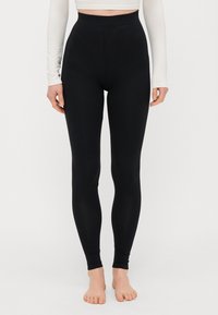 Leggings noirs taille haute avec une texture extensible et une coupe ajustée, sans coutures visibles et avec une finition lisse.
