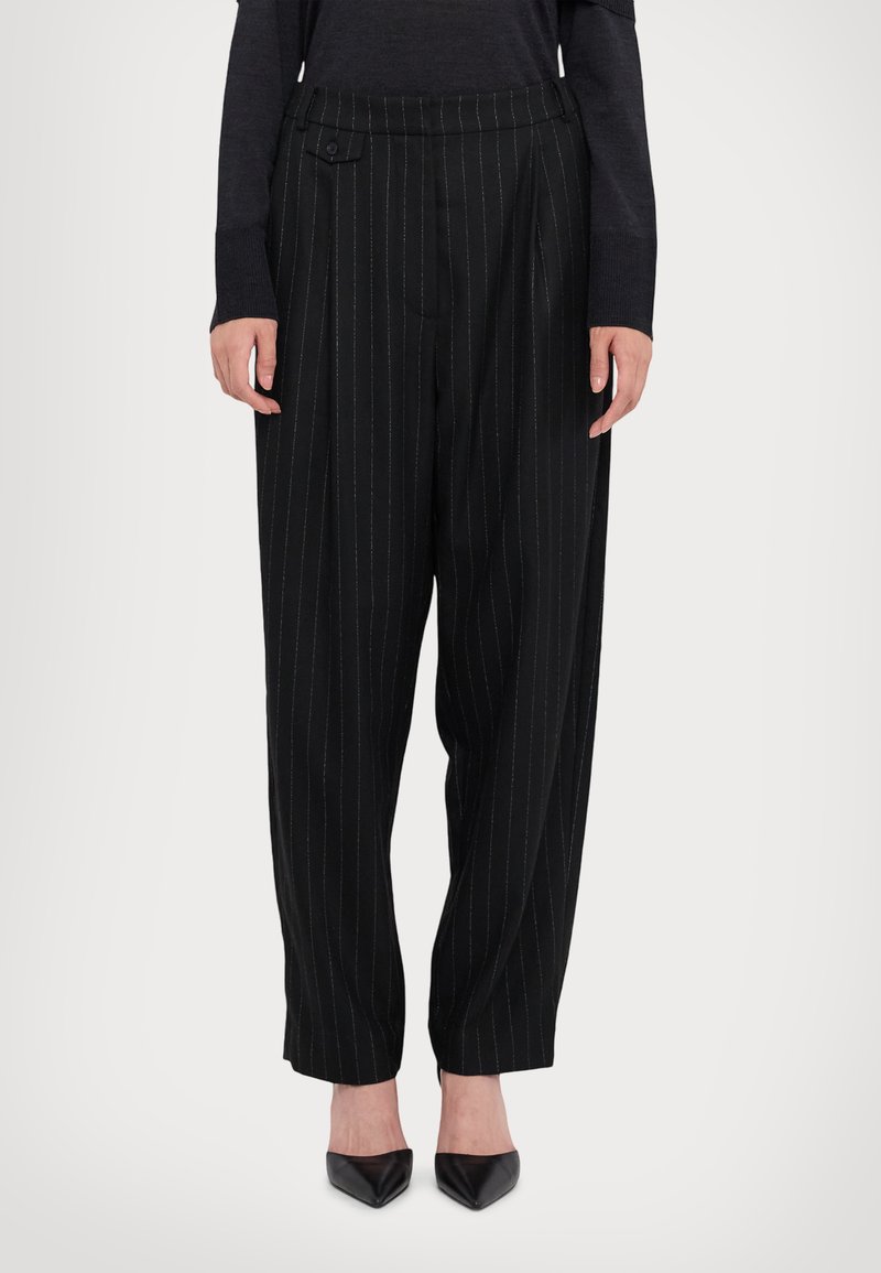 Pantalons noirs à rayures avec une taille haute, dotés de plis et d'un détail de bouton. Le tissu a une texture lisse. Portés avec des talons aiguilles noirs.