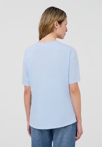 T-shirt in cotone azzurro chiaro con maniche corte, scollatura rotonda e vestibilità morbida. Texture liscia, design essenziale e orlo posteriore più lungo.