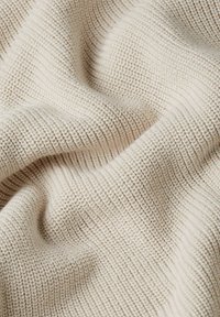 Tessuto color crema con una superficie strutturata e a coste. Il materiale è morbido e leggermente elastico, con linee verticali in tutto il suo spessore.