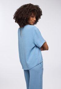 Top azzurro chiaro con texture e maniche corte, dotato di un dettaglio a chiave sul retro. Abbinato a pantaloni azzurro chiaro coordinati per un look armonioso.