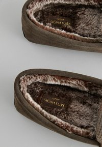 Mørkebrune ruskindsslippers med en luksuriøs faux fur foring. Har en blød tekstur, rund form og et diskret guldmærke indeni.