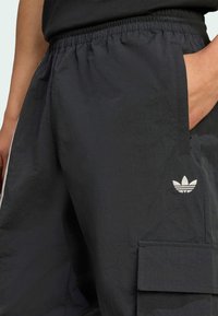 Čierne ľahké cargo nohavice s elastickým pásom, obsahujú bočné vrecká a malé biele logo Adidas trefoil na nohavici.