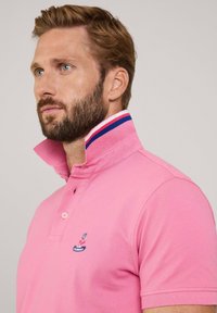 Polo shirt rosa realizzato in tessuto testurizzato, con colletto a bottoni, scollatura a righe in contrasto e un piccolo logo sul petto.