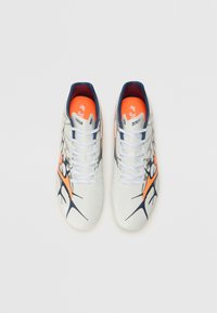 Zapatillas deportivas blancas con un acabado brillante, que presentan diseños abstractos en negro y naranja, puntera redonda y cordones blancos, con un cuello en azul marino.