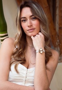 Montre à bracelet clair, avec un motif floral en métal doré. Le bracelet est lisse, complétant la forme élégante de la montre.