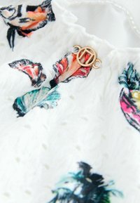 Bavlnená látka s kvetinovým vzorom v bielej farbe s farebnými motýlikmi; textúrovaný povrch; zlaté kovanie s detailom okrúhlej pracky.