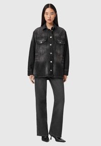 Camisa de ganga preta com botões de pressão, dois bolsos frontais e um corte descontraído, acompanhada de jeans largos pretos combinando.