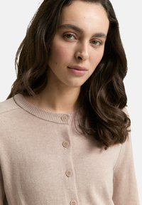 Lichtroze, gebreide cardigan met een ronde halslijn en zes knopen. Heeft een zachte textuur en geribbelde accenten bij de kraag.