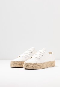 Sneakers bianchi in tela con suola piattaforma in corda intrecciata. Presentano punta rotonda, chiusura con lacci e una texture sottile sul materiale superiore.