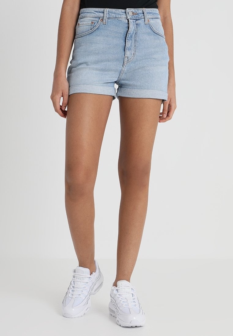 Shorts de mezclilla azul claro con dobladillo vuelto, diseño de cinco bolsillos y cintura ajustada. Se usan con zapatillas deportivas blancas.