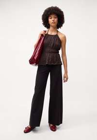 Haut en halter texturé marron avec une taille peplum, associé à un pantalon large noir et des ballerines rouges, avec un sac rouge assorti.