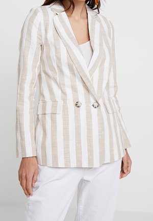 Beige and white vertical striped double-breasted blazer with lapels, front flap pockets, worn over a white top and white pants.