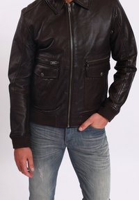 Hnědá kožená bunda se zipem vpředu, dvěma náprsními kapsami, žebrovanými manžetami a spodním lemem, hladkou texturou a klasickým límečkem.