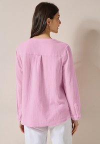 Camicia rosa chiaro a maniche lunghe realizzata in tessuto testurizzato, con una piega sulla schiena e polsini con bottoni, dal taglio rilassato e collo rotondo.