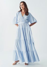 Světle modré maxi šaty s překládaným designem, krátkými nabíranými rukávy, vrstvenými volány a stahováním v pase; vyrobené z měkké, prodyšné látky.