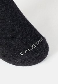 Zbliżenie czarnej skarpetki z białym napisem "CALZITALY" wyszytym na gładkim białym tle.