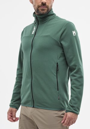 Green fleece jacket with high collar, zippered front, side pockets, textured fabric, and contrasting black zipper detail. Logo on sleeve.