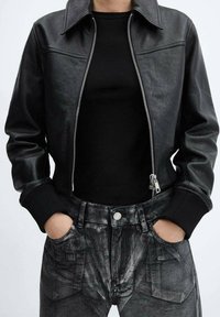 Chaqueta bomber de cuero negro con cremallera frontal, puños y cuello acanalados. Combinada con pantalones negros texturizados con bolsillos delanteros.