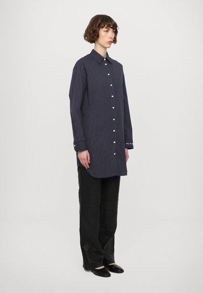 Camisa a rayas de botones en un oscuro azul marino, con cuello, botones en el frente y mangas largas con puños en contraste. Combínala con pantalones anchos negros.