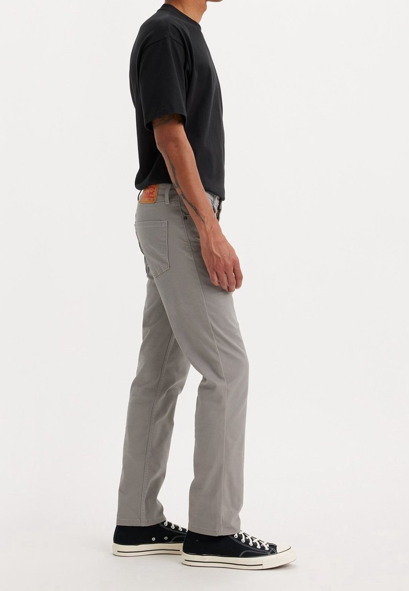 Pantalones rectos grises con una textura sutil, combinados con una camisa negra de manga corta y deportivos negros, tomados de lado.