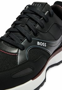 Schwarze Sneaker aus Mesh- und Lederstoffen. Verfügt über eine dicke weiße Sohle, ein Schnürdesign und ein weißes "BOSS"-Logo an der Seite.