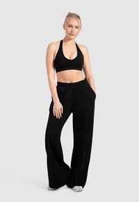 Zwarte sportbeha en zwarte, loszittende joggingbroek met zijzakken. Voorzien van een brede tailleband en contrasterende stiksels.