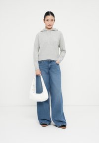 Grau gestrickter Kapuzenpullover mit einer Fronttasche, kombiniert mit weit geschnittenen blauen Jeans. Weiße Handtasche mit Nietenverzierung.
