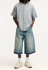 Camisa de botones de manga corta gris claro, culottes de mezclilla azul holgados y zapatillas blancas con acentos beiges.