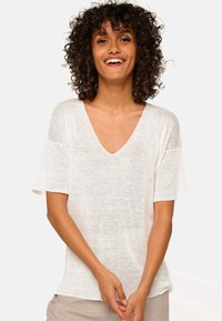 Short-sleeve, v-neck top in lightweight, sheer white fabric with a relaxed fit and slightly frayed sleeve edges.