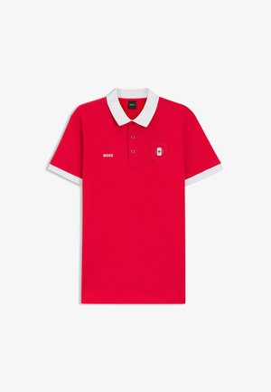 Camiseta polo roja con cuello y bordes de las mangas blancos, con el logo "BOSS" en el pecho izquierdo y un pequeño emblema de la bandera canadiense en el derecho.