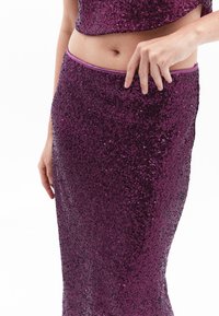 Fialový korálkový dvoudílný outfit obsahující crop top a přiléhavou sukni s hladkým pasem a třpytivou texturou.