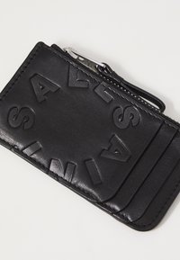 Czarny skórzany portfel-karta z wytłoczonymi literami, z zamkiem błyskawicznym oraz wieloma kieszonkami na karty. Gładka tekstura i minimalistyczny design.