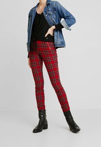 Jeansjacke, schwarzes Top mit Krawatte vorne, rote karierte Skinny-Hose mit Muster und schwarze Knöchelstiefel mit seitlichem Reißverschluss.
