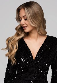 Robe noire en sequins avec un décolleté en V profond, des manches longues et une surface texturée. Comprend des détails étincelants et un design à taille froncée.