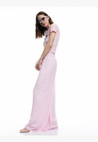 Lichtroze wijde broek met een smocked tailleband, gecombineerd met een roze top met korte mouwen en grafische tekst. Zonnebril maakt de look compleet.